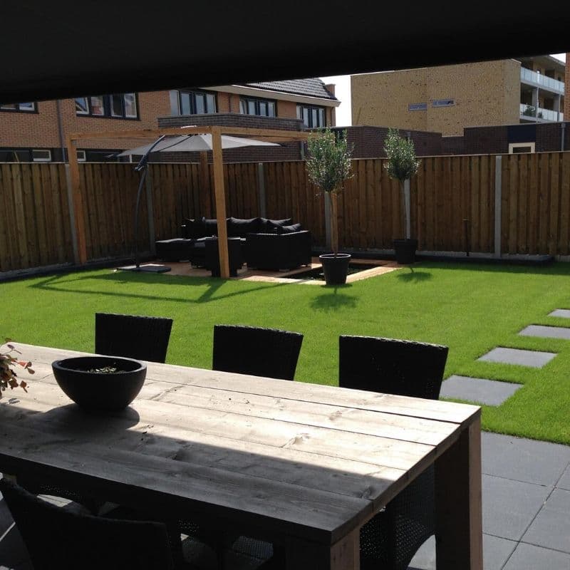 Achtertuin met kunstgras, houten schutting, loungeset en bestrate looppaden